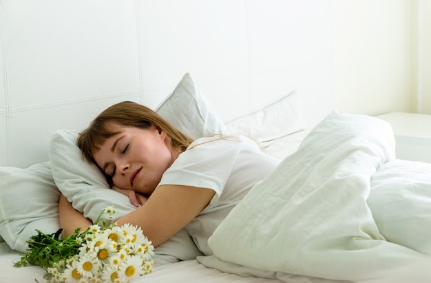 Jonge mooie vrouwenslaap in bed met madeliefjesbloemen