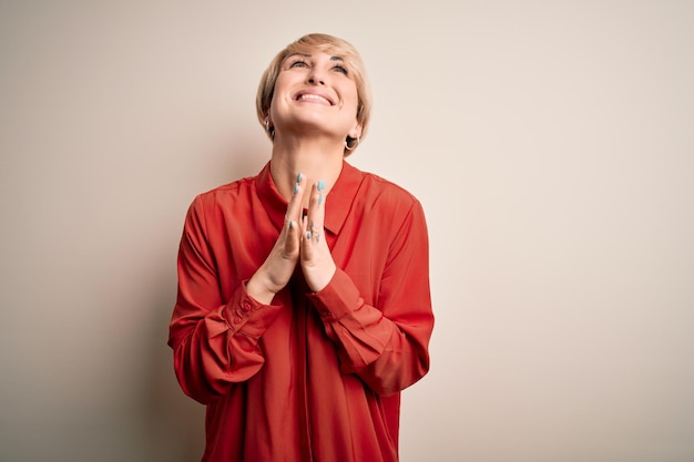 Jonge mooie zaken blonde vrouw met kort haar staande over geïsoleerde achtergrond bedelend en biddend met de handen samen met hoopvolle uitdrukking op het gezicht erg emotioneel en bezorgd