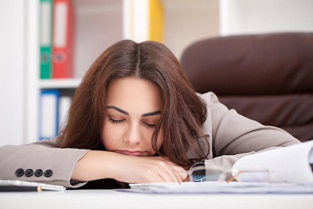 Jonge, mooie zakenvrouw die aan stress lijdt terwijl ze op kantoor om hulp vraagt en zich moe voelt