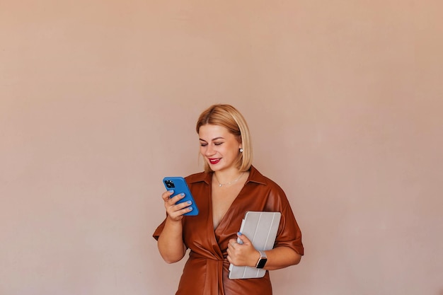 Jonge mooie zakenvrouw in een bruine jurk praten aan de telefoon met een laptop in haar handen