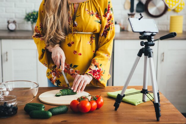 Foto jonge mooie zwangere meid blogger maakt een video van een salade recept op de camera van een smartphone