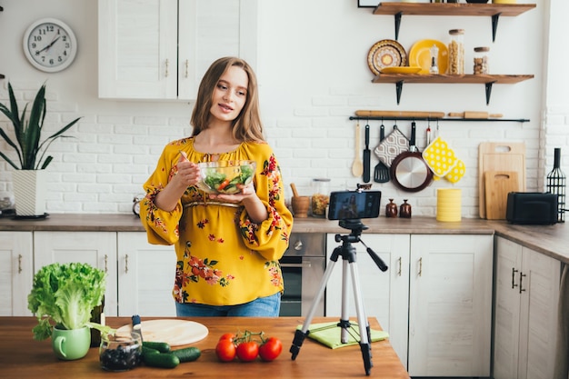 Jonge mooie zwangere meid blogger maakt een video van een salade recept op de camera van een smartphone