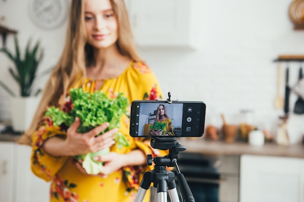 Jonge mooie zwangere meid blogger maakt een video van een salade recept op de camera van een smartphone