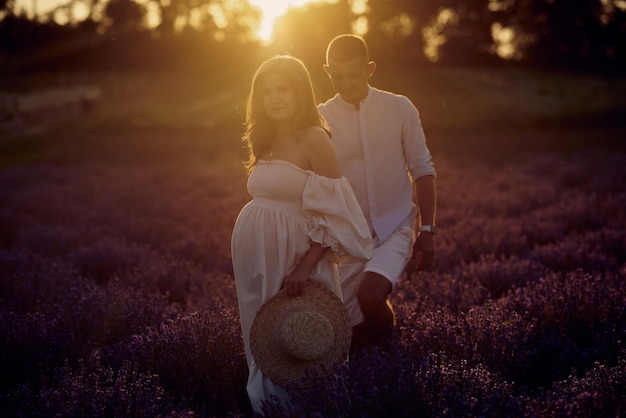 Jonge mooie zwangere paar wandelen op een lavendelveld bij zonsondergang Happy family concept