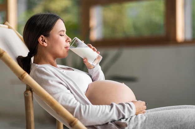 Jonge mooie zwangere vrouw die in de stoel rust en melk uit glas drinkt