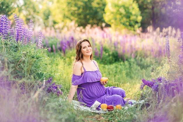 Jonge mooie zwangere vrouw in een paarse jurk zit in een veld met lupine Picknick in de natuur