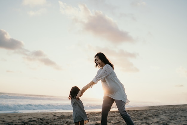 Jonge mooie zwangere vrouw met haar kleine schattige dochter spelen in het strand