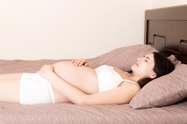 Jonge mooie zwangere vrouw met pijn zittend op bed in de slaapkamer die zich voorbereidt om te bevallen