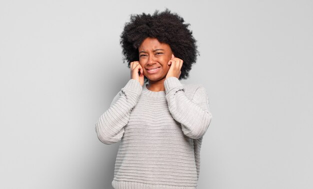 jonge mooie zwarte vrouw die haar oren bedekt. Luid geluid concept