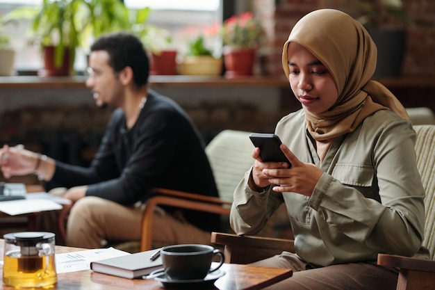 Jonge moslim zakenvrouw in hijab messaging in smartphone
