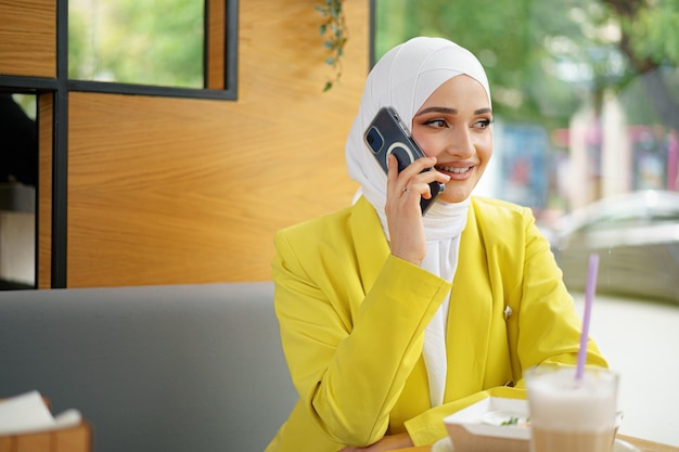 Jonge moslim zakenvrouw in hoofddoek zitten in café en praten aan de telefoon