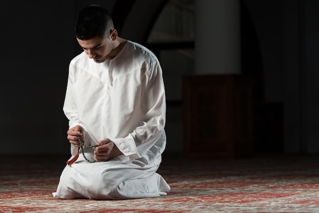 Jonge moslimman die traditioneel tot God bidt terwijl hij een traditionele pet draagt