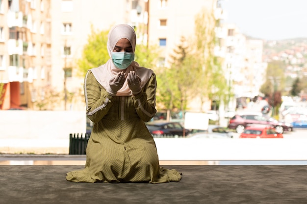 Jonge moslimvrouw die buiten bidt met een beschermend masker en handschoenen