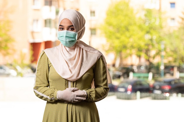 Jonge moslimvrouw die buiten bidt met een beschermend masker en handschoenen