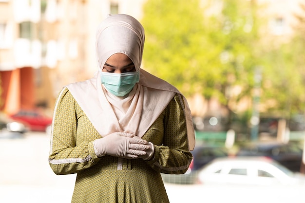 Jonge moslimvrouw die buiten bidt met een beschermend masker en handschoenen