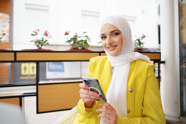 Jonge moslimvrouw in hijab die haar smartphone in café gebruikt