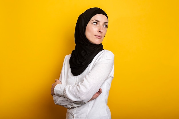 Jonge moslimvrouw in hijab kijkt opzij en kijkt terug tegen een gele