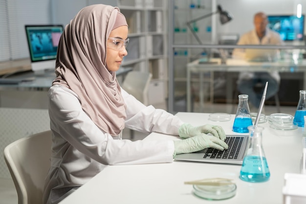 Jonge moslimvrouw in hijab laboratoriumjas beschermende brillen en handschoenen