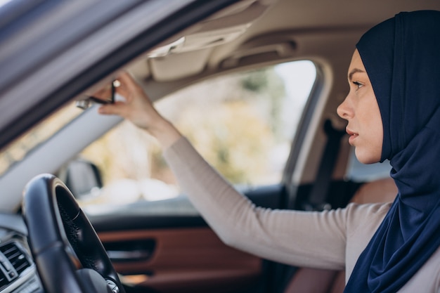 Jonge moslimvrouw zit in haar auto en kijkt in de spiegel