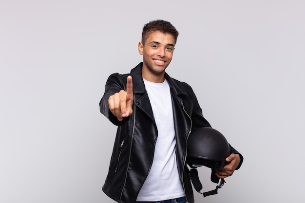 Jonge motorrijder die trots en zelfverzekerd glimlacht en nummer één triomfantelijk laat poseren, zich een leider voelt
