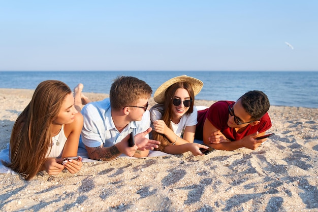 Jonge multi-etnische groep millennials ontspannen op het strandlaken in de buurt van zee op wit zand stylish