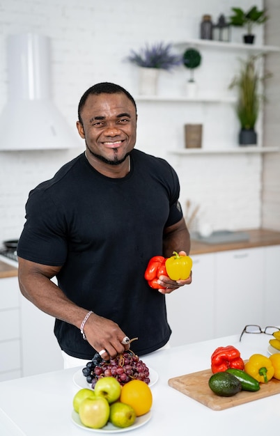 Jonge multiraciale man die in de buurt van een tafel vol met verschillende groenten en fruit staat en kookt Moderne lichte keuken