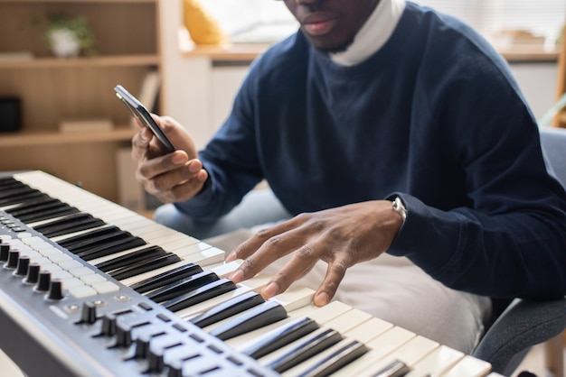 Jonge muziekleraar met smartphone die toetsen van pianotoetsenbord aanraakt