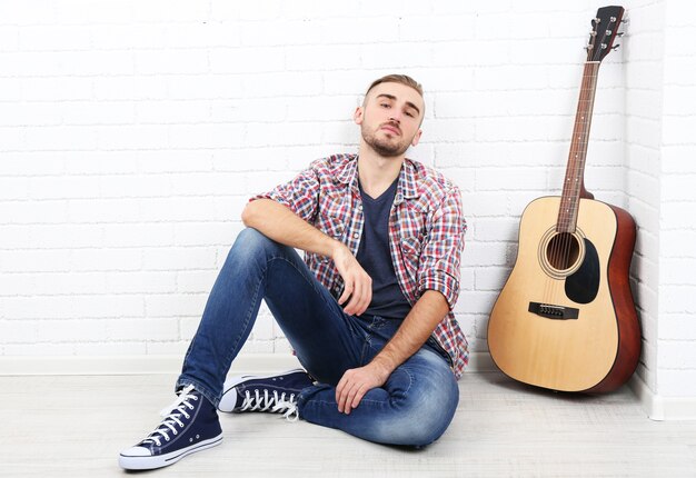 Jonge muzikant met gitaar op lichte muur