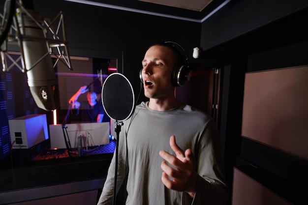 Jonge muzikant zingt in een microfoon terwijl hij nummers neerlegt in een muziekstudio