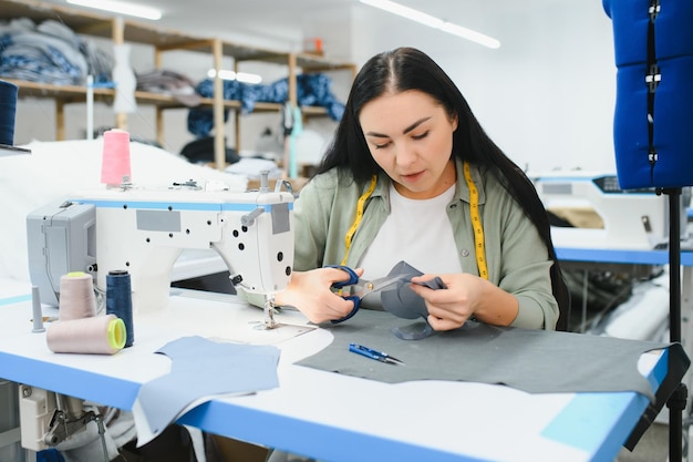 Jonge naaister vrouw naait kleding op werktafel Lachende naaister en haar hand close-up in werkplaats