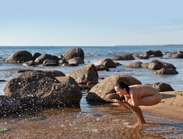 Jonge naakte vrouw die in zee staat en met water speelt