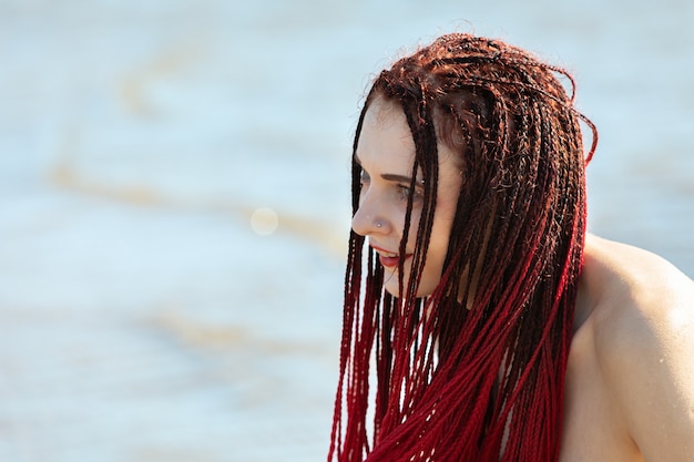 Jonge naakte vrouw met dieprode dreadlocks geniet van de natuur aan zee