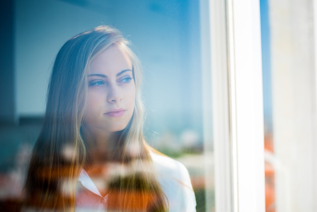 Jonge nadenkende vrouw die door het venster kijkt