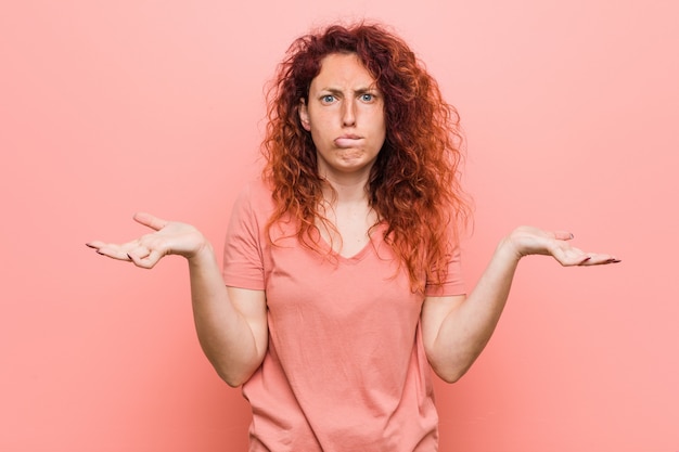 Foto jonge natuurlijke en authentieke redhead vrouw verward en twijfelachtig schouderophalend schouders om een exemplaarruimte te houden.