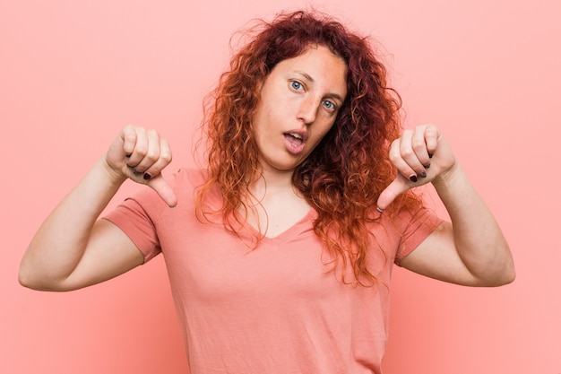 Jonge natuurlijke en authentieke roodharige vrouw die duim naar beneden toont en afkeer uitdrukt.