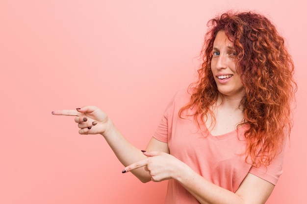 Jonge natuurlijke en authentieke roodharige vrouw opgewonden wijzend met wijsvingers weg.