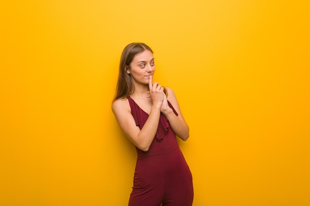 Jonge natuurlijke vrouw die een rode jurk draagt op een oranje muur