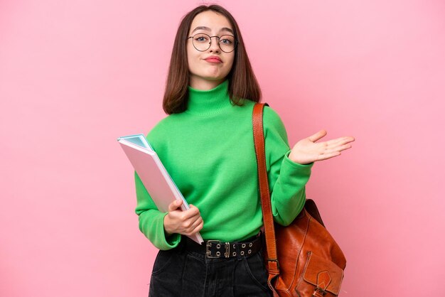 Jonge Oekraïense studente die op roze achtergrond wordt geïsoleerd die twijfels heeft terwijl het opsteken van handen