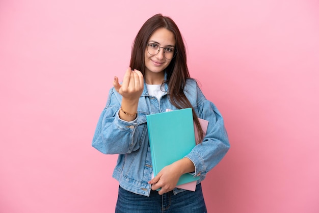 Jonge oekraïense studentenvrouw geïsoleerd op roze achtergrond die uitnodigt om met de hand te komen blij dat je bent gekomen