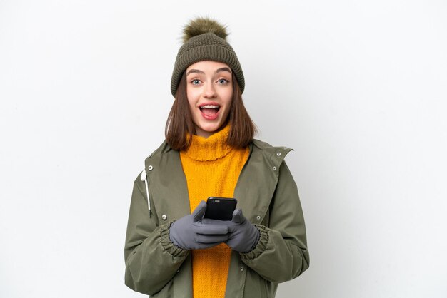 Jonge Oekraïense vrouw draagt winterjas geïsoleerd op een witte achtergrond verrast en stuurt een bericht