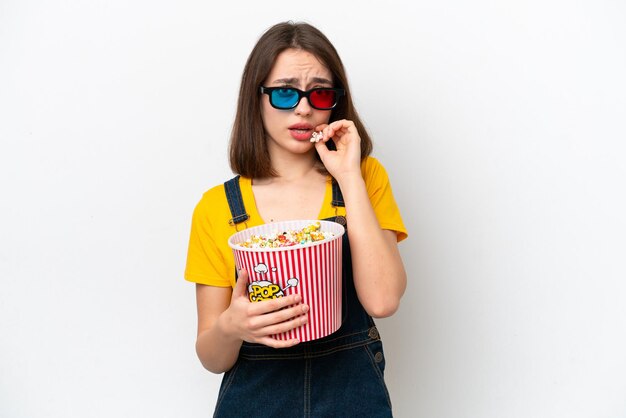 Jonge Oekraïense vrouw geïsoleerd op een witte achtergrond met 3D-bril en met een grote emmer popcorns