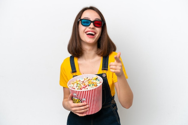 Jonge Oekraïense vrouw geïsoleerd op een witte achtergrond met een 3D-bril en een grote emmer popcorns vasthoudend terwijl ze naar voren wijst