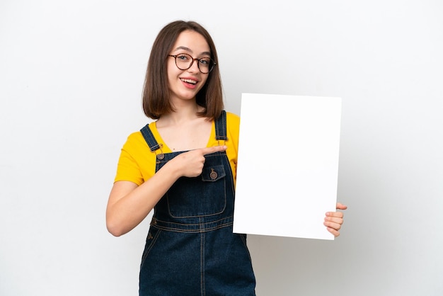 Jonge Oekraïense vrouw geïsoleerd op een witte achtergrond met een leeg bordje met gelukkige uitdrukking en erop wijzend