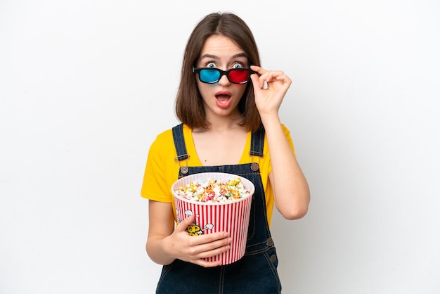 Jonge Oekraïense vrouw geïsoleerd op een witte achtergrond verrast met 3D-bril en met een grote emmer popcorns