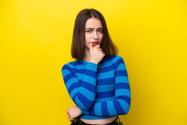 Jonge Oekraïense vrouw geïsoleerd op gele achtergrond met twijfels