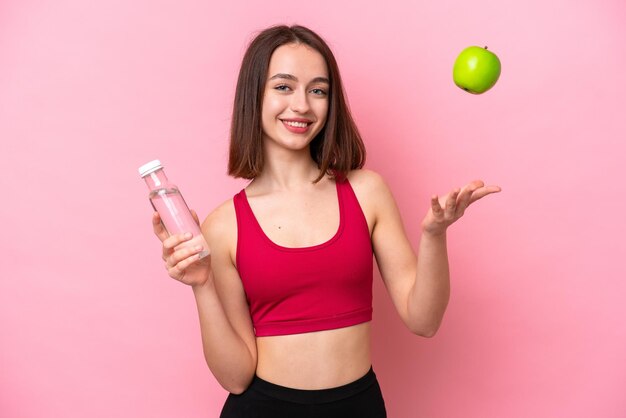 Jonge oekraïense vrouw geïsoleerd op roze achtergrond met een appel en met een fles water