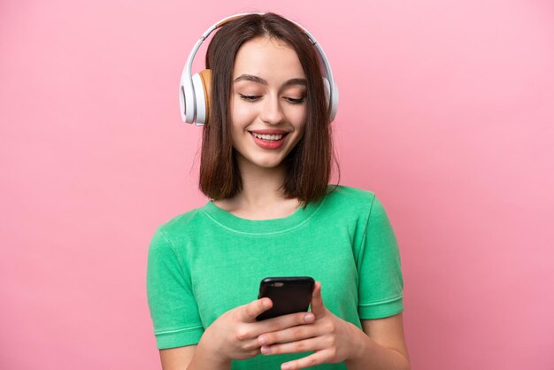 Jonge Oekraïense vrouw geïsoleerd op roze achtergrond muziek luisteren en kijken naar mobiel
