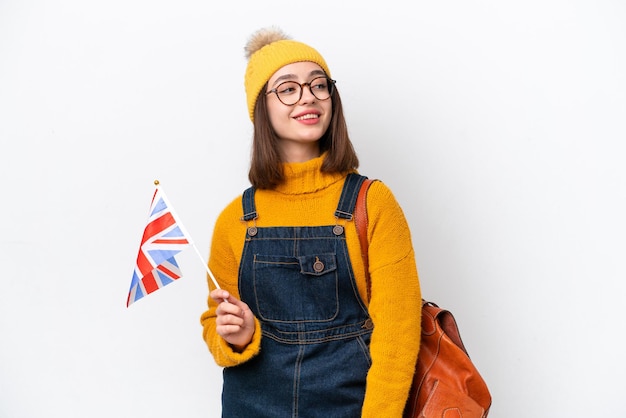 Jonge Oekraïense vrouw met een vlag van het Verenigd Koninkrijk die op een witte achtergrond wordt geïsoleerd en naar de zijkant kijkt en glimlacht