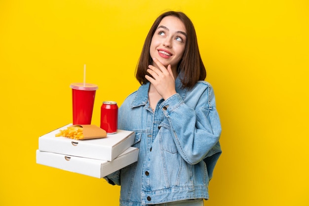 Jonge Oekraïense vrouw met fastfood geïsoleerd op een gele achtergrond terwijl ze glimlacht