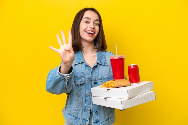 Jonge Oekraïense vrouw met fastfood geïsoleerd op gele achtergrond gelukkig en vier tellen met vingers